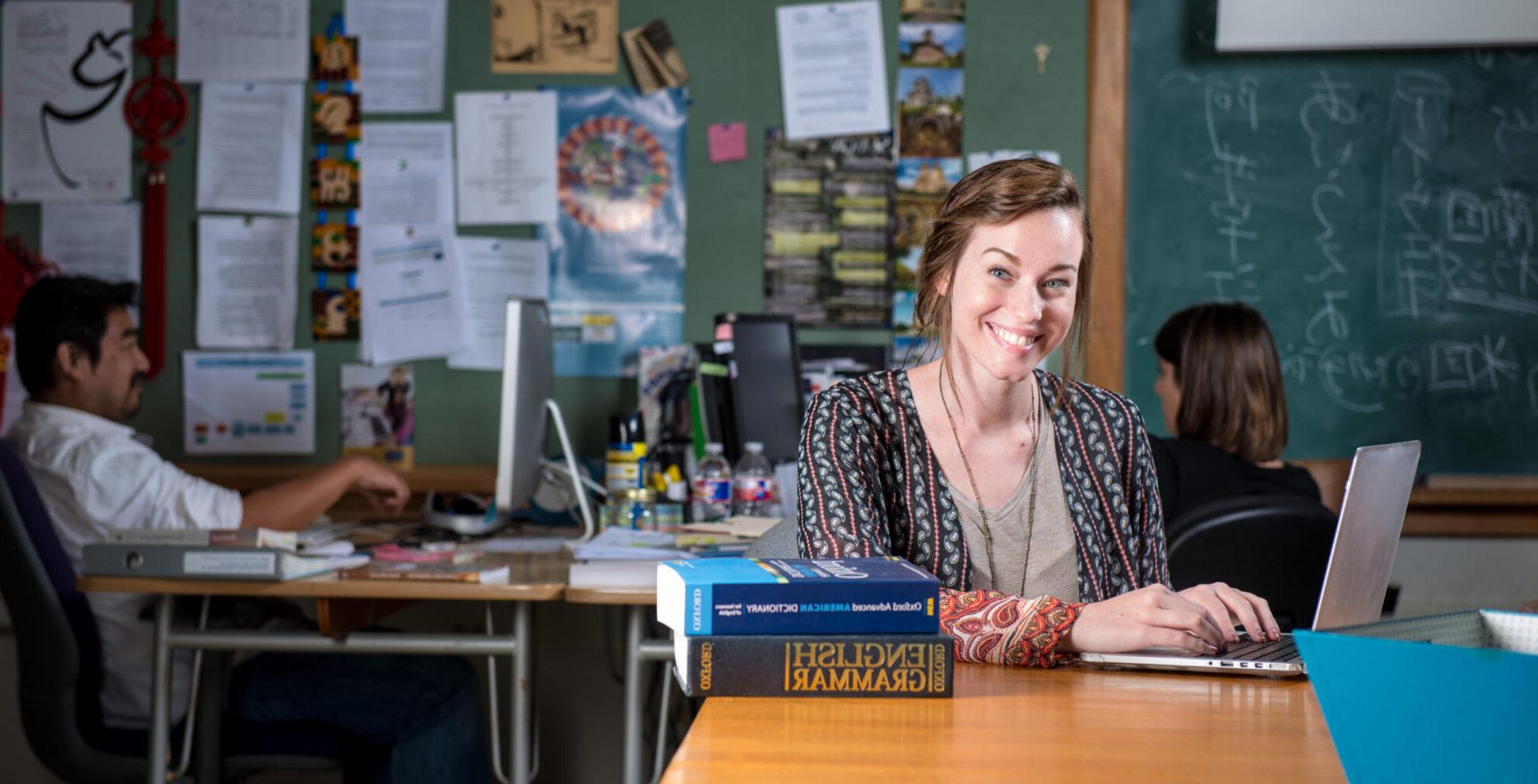 Young woman smiling at desk with laptop and English grammar books