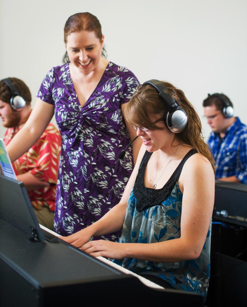 student playing keyboard with instructor observing with smile.