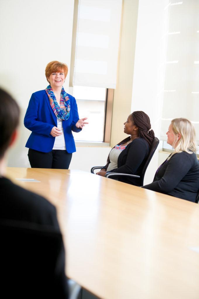 Business dressed woman speaking to group around a large table.
