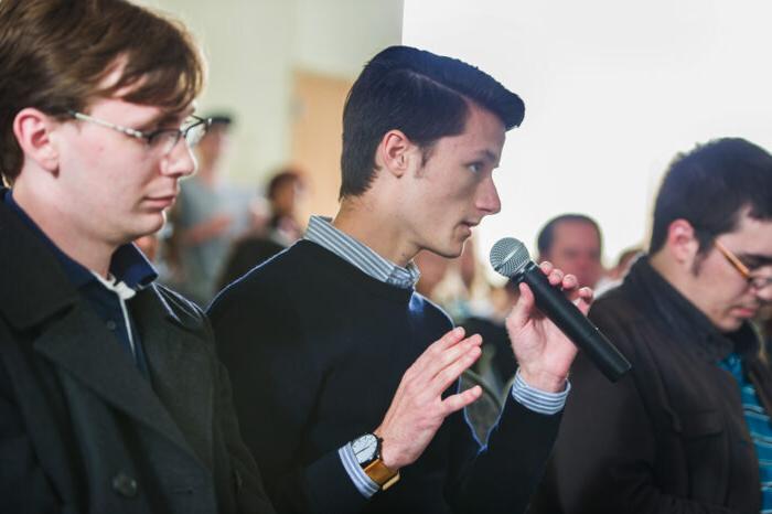 Man speaking into a handheld microphone in a town-hall style meeting.