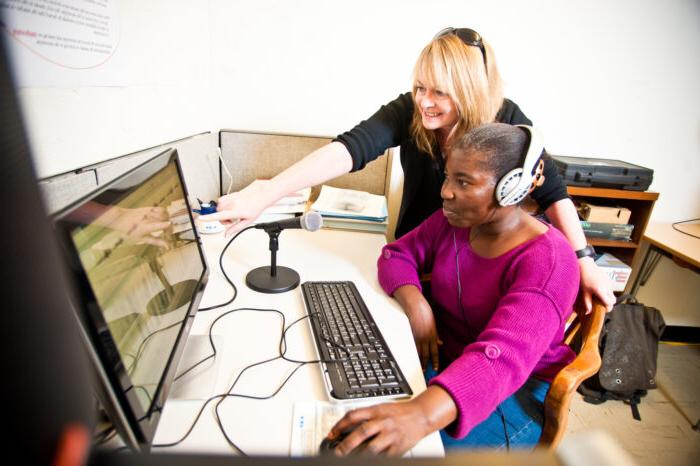 An educator teaching a student who is setting at a computer while wearing headphones.