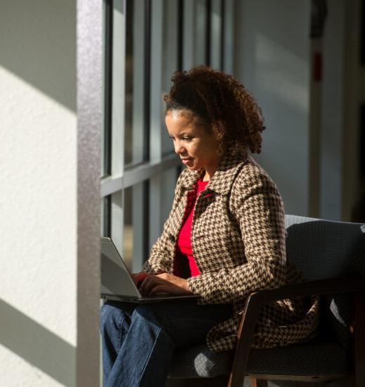 Woman working on laptop seated facing windows.