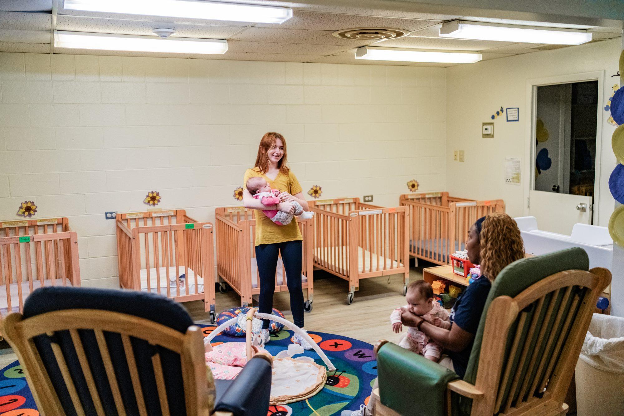 Infant room with two employees holding and playing with infants.