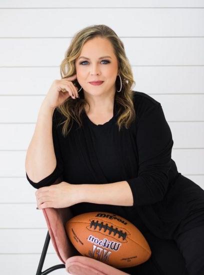 A woman looks at the viewer while leaning casually in a chair with a football