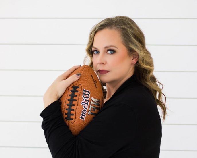 A woman poses with a football while looking at the viewer