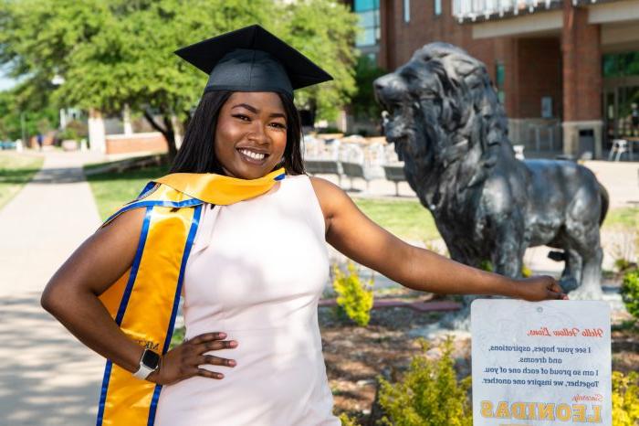 Graduate poses in graduation cap and stole with Lion statue in background.